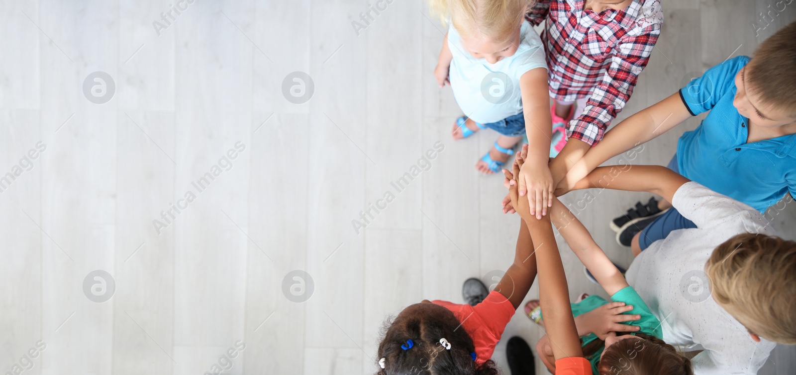 Photo of Little children putting their hands together indoors, top view. Unity concept