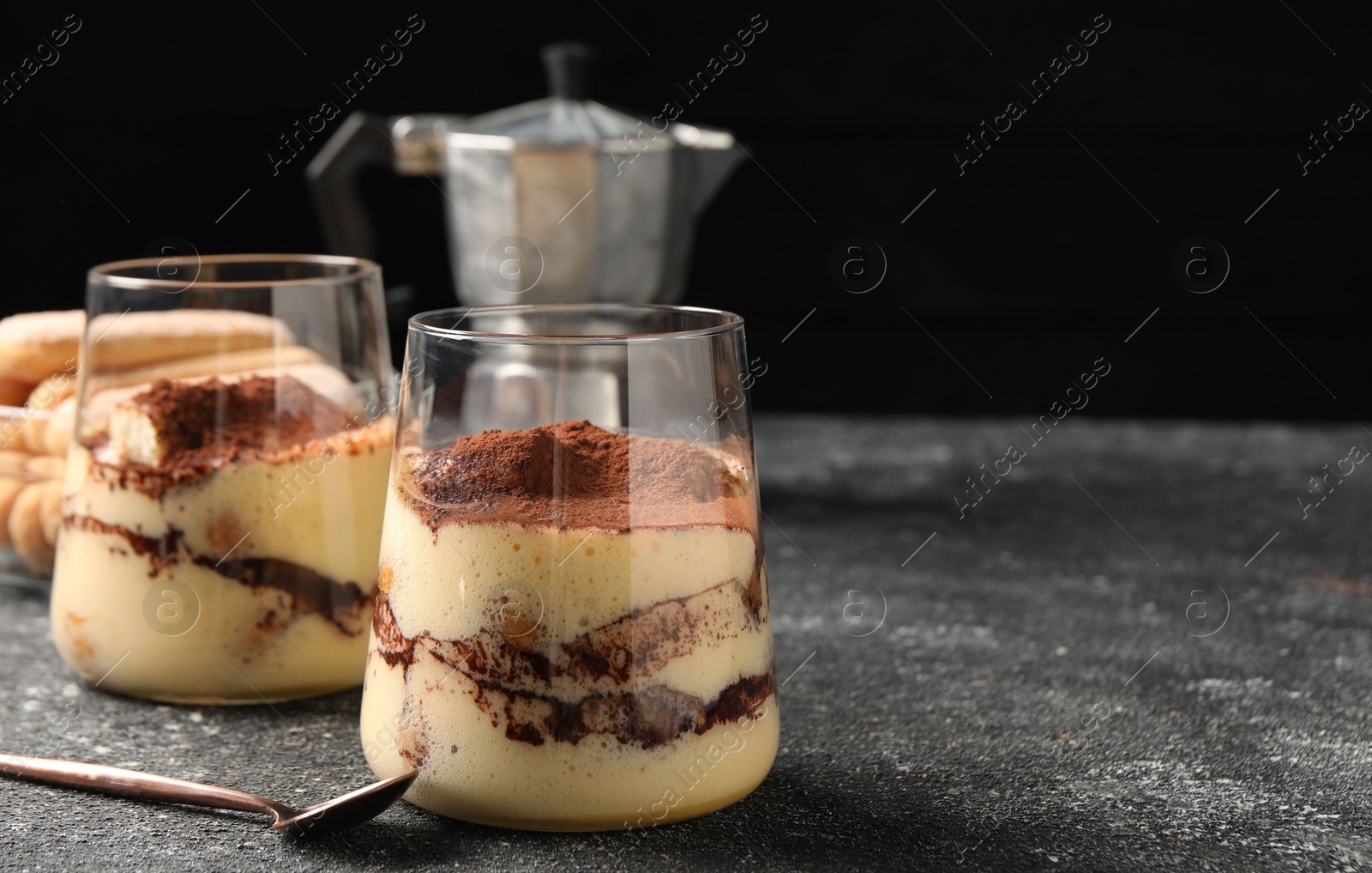 Photo of Delicious tiramisu in glasses and spoon on grey textured table, closeup. Space for text