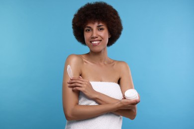 Photo of Beautiful young woman applying body cream onto arm on light blue background