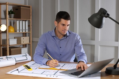 Architect working with construction drawings and laptop in office