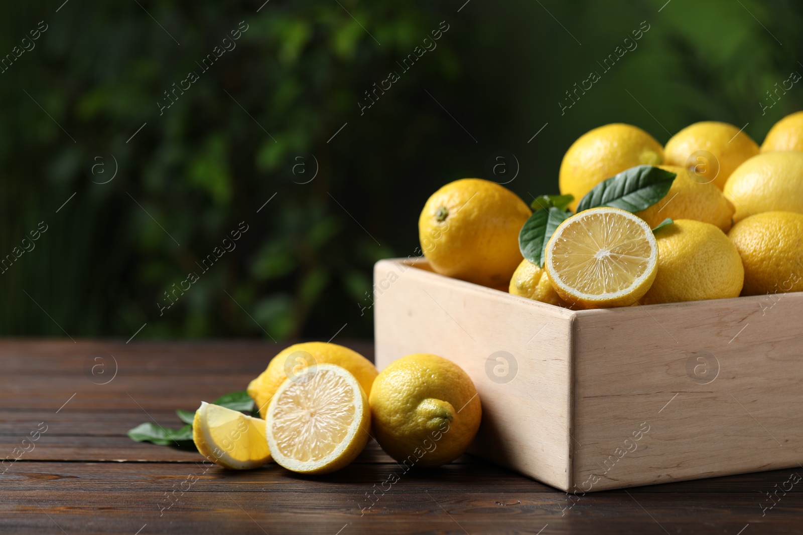 Photo of Fresh lemons in crate on wooden table. Space for text