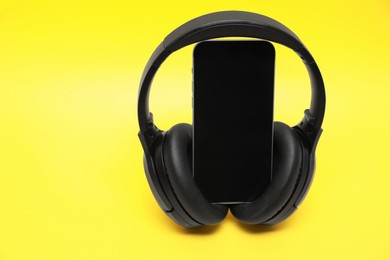 Photo of Modern wireless headphones and smartphone on yellow background