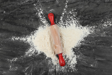 Flour and rolling pin on grey marble table, top view