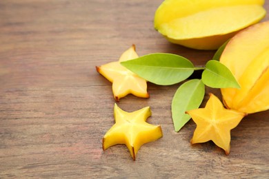 Photo of Cut and whole delicious ripe carambolas with leaves on wooden table, closeup