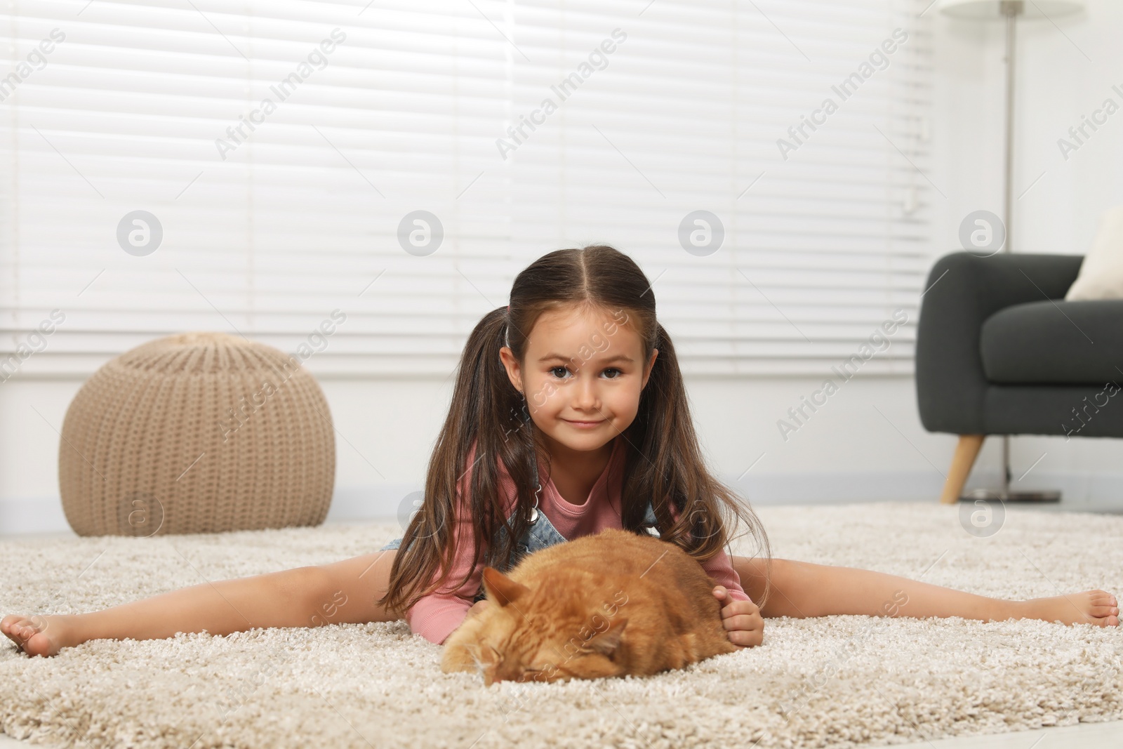 Photo of Smiling little girl and cute ginger cat on carpet at home