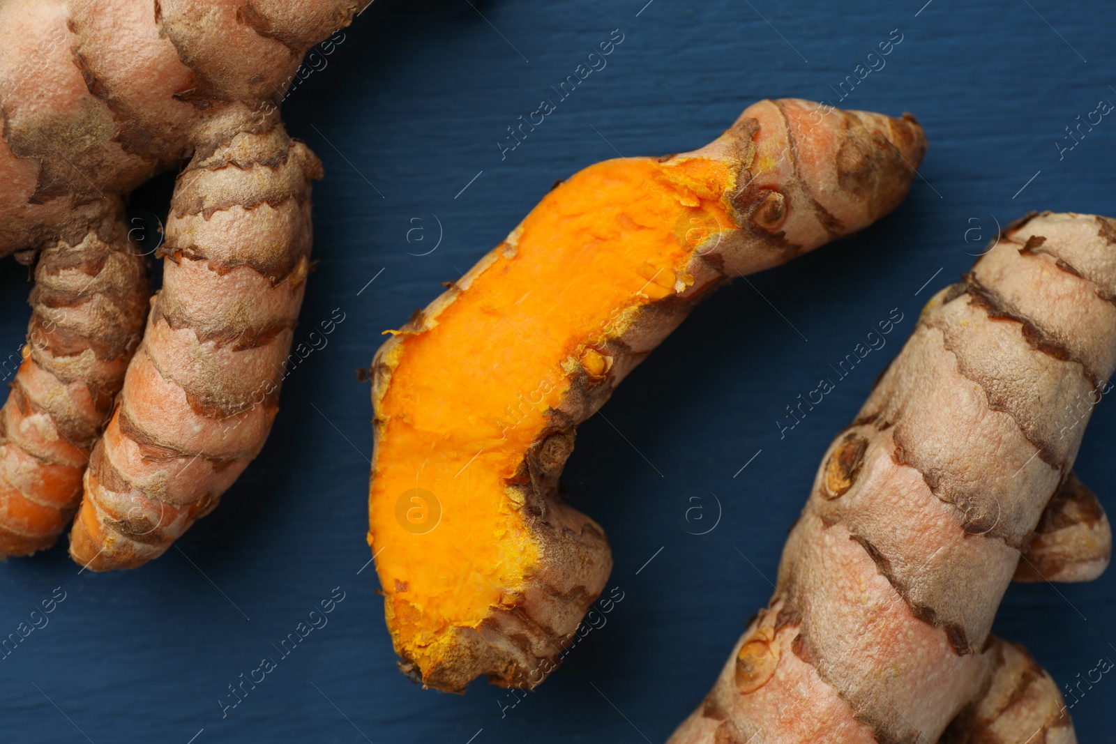 Photo of Raw turmeric roots on blue wooden table, flat lay