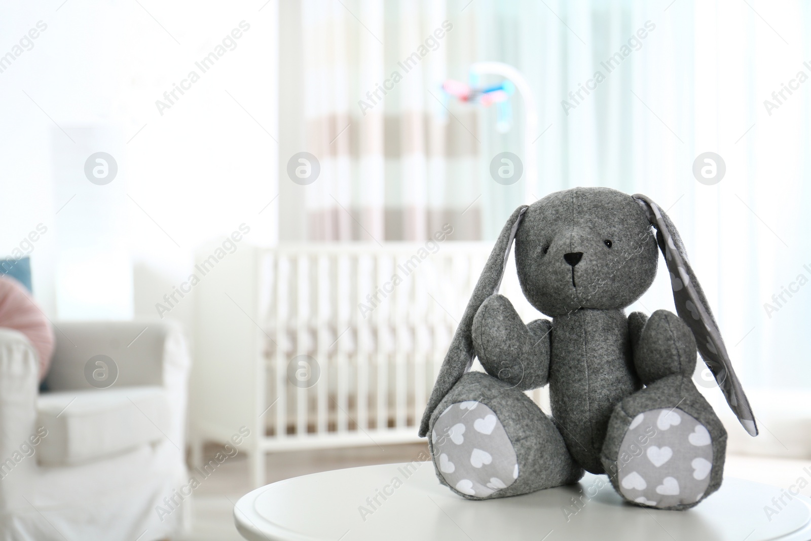 Photo of Stuffed toy bunny on table in baby room interior. Space for text