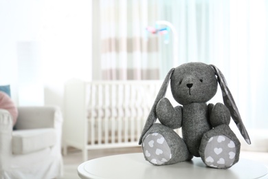 Stuffed toy bunny on table in baby room interior. Space for text