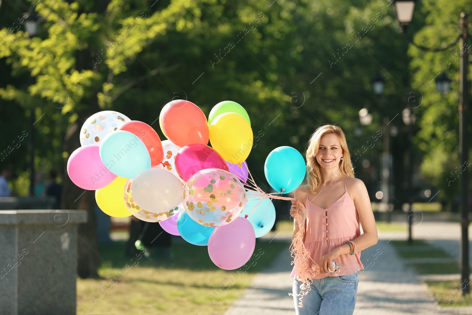 Photo of Young woman with colorful balloons outdoors on sunny day