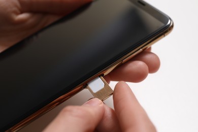 Photo of Woman putting SIM card tray in smartphone at white table, closeup