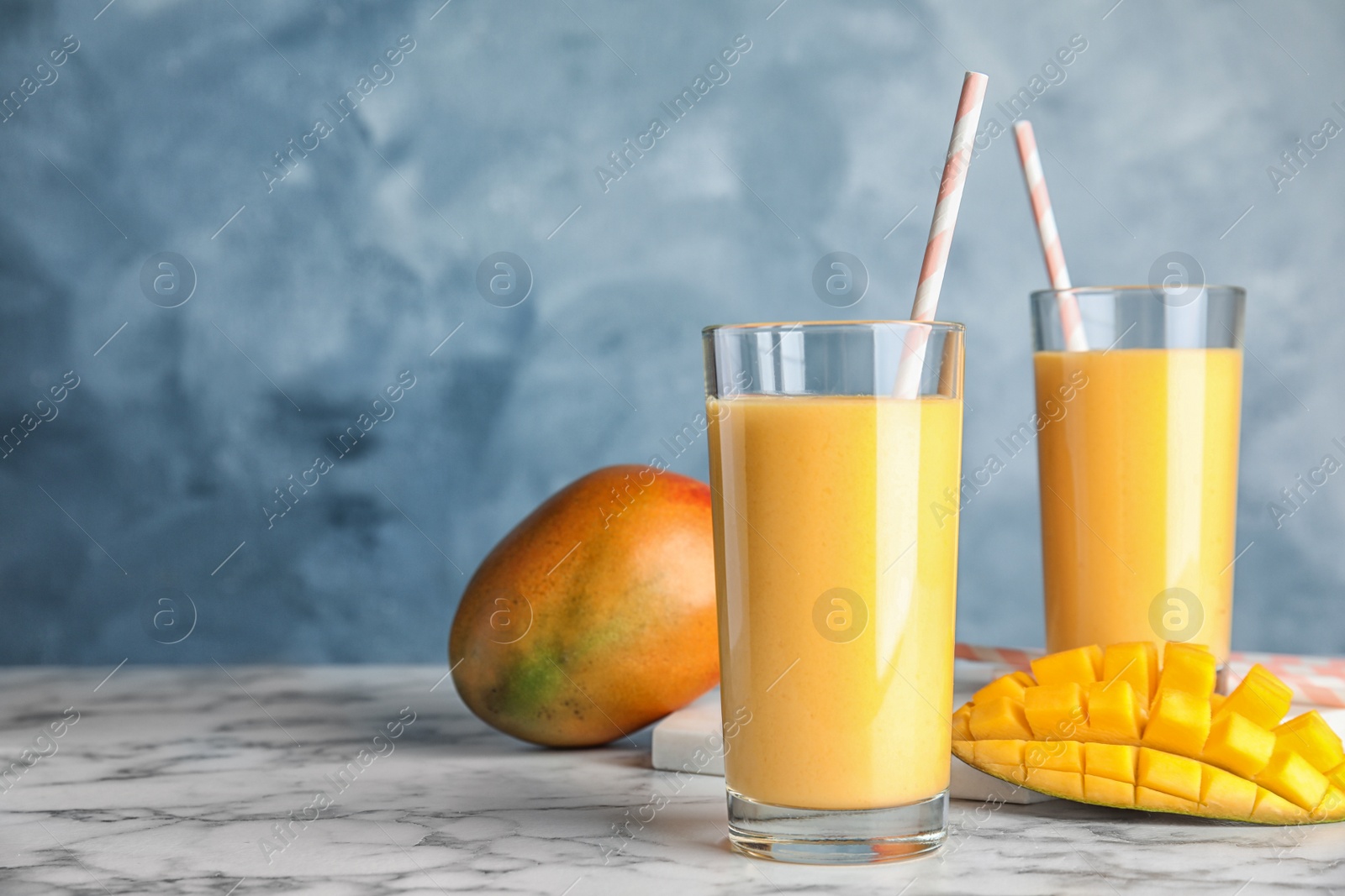 Photo of Glasses of fresh mango drink and fruits on table against color background. Space for text