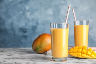 Photo of Glasses of fresh mango drink and fruits on table against color background. Space for text