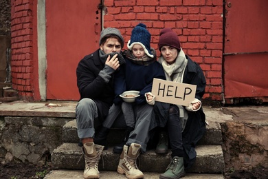 Photo of Poor young family with HELP sign on dirty street