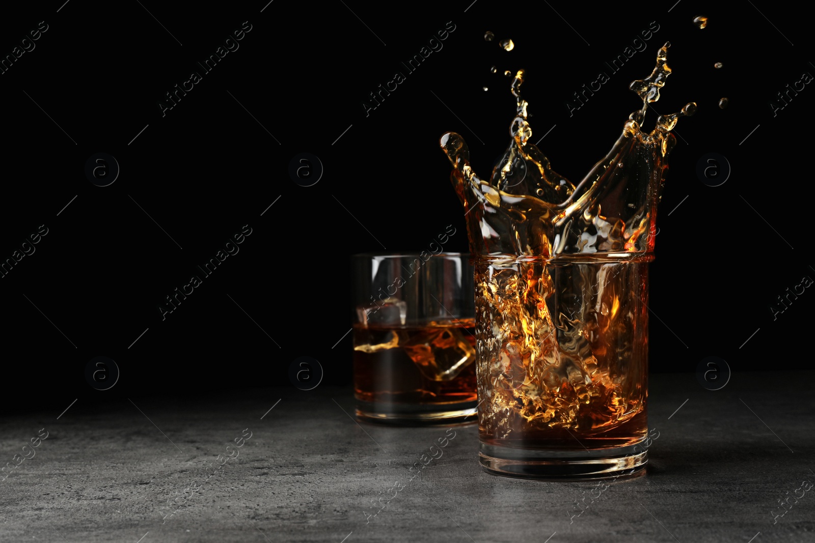 Photo of Splashing golden whiskey in glass with ice cubes on table. Space for text