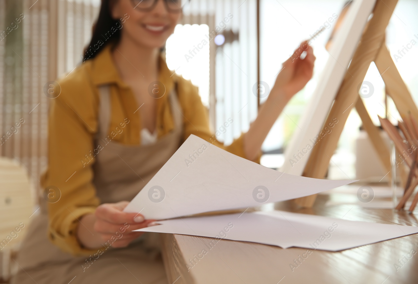 Photo of Young woman taking sheet of paper for drawing at table indoors, closeup