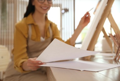 Photo of Young woman taking sheet of paper for drawing at table indoors, closeup