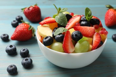 Photo of Tasty fruit salad in bowl and ingredients on light blue wooden table, closeup
