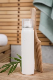Photo of Dry shampoo spray, green leaves and comb on wooden table in bathroom