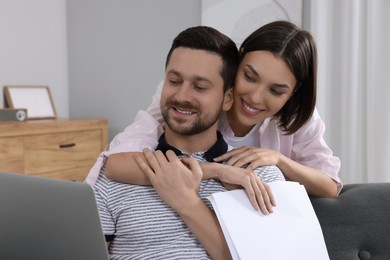 Photo of Young couple with laptop and papers discussing pension plan indoors