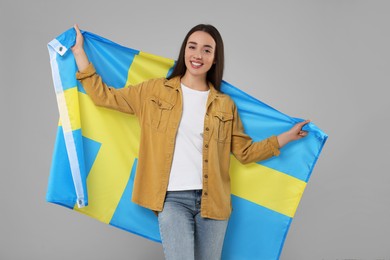 Photo of Young woman holding flag of Sweden on light grey background