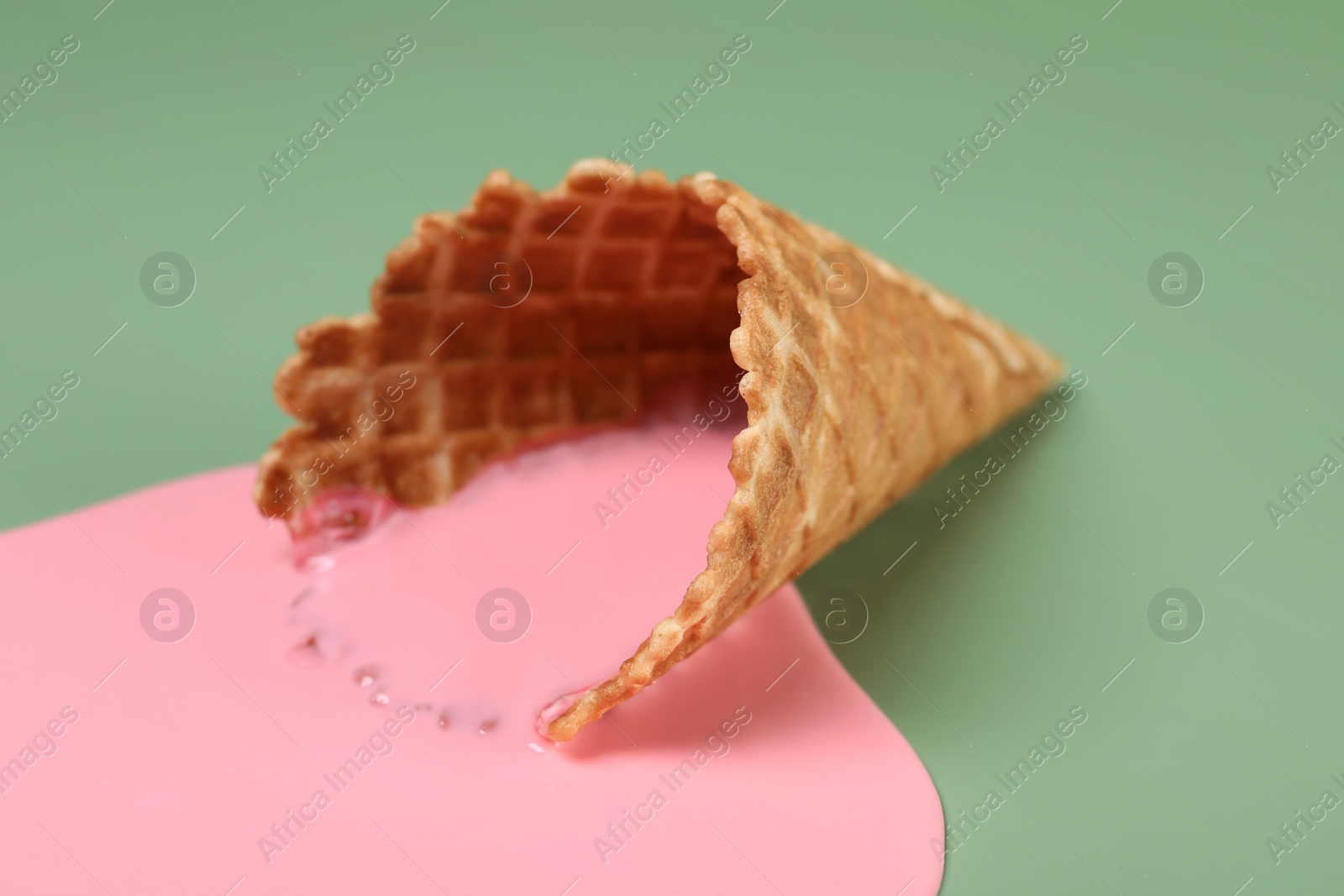 Photo of Melted ice cream and wafer cone on green background, closeup
