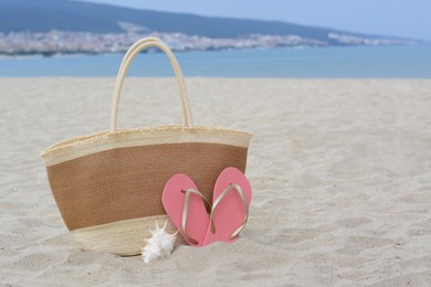 Photo of Stylish straw bag, flip flops and shell on sand near sea, space for text. Beach accessories