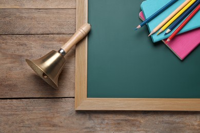 Photo of Golden bell, green chalkboard and stationery on wooden background, flat lay. School days