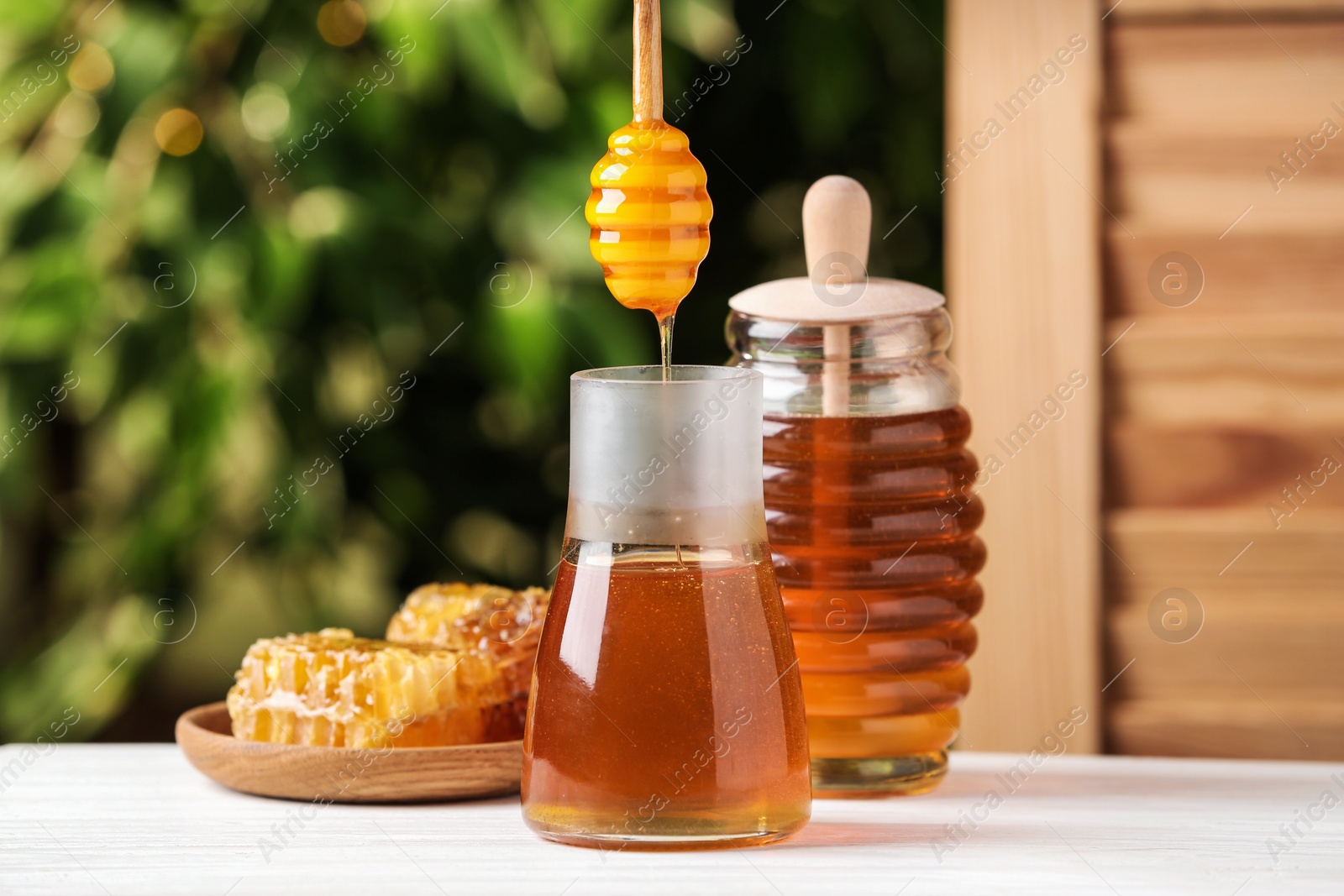 Photo of Dripping tasty honey from dipper into jar on white wooden table