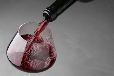 Photo of Pouring tasty red wine in glass at gray table, closeup. Space for text