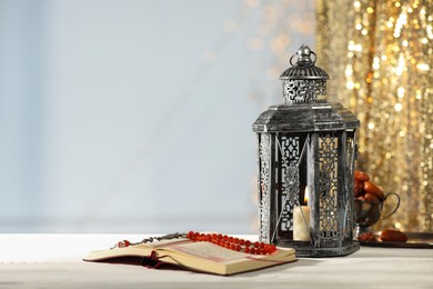 Arabic lantern, Quran, misbaha and dates on table against blurred lights, space for text