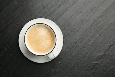 Tasty cappuccino in cup and saucer on dark textured table, top view. Space for text