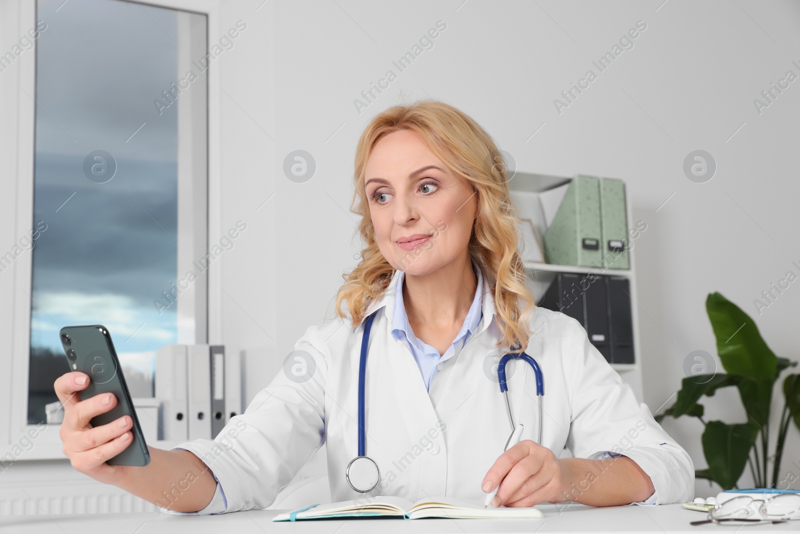 Photo of Doctor with smartphone and notebook consulting patient in clinic. Online medicine concept