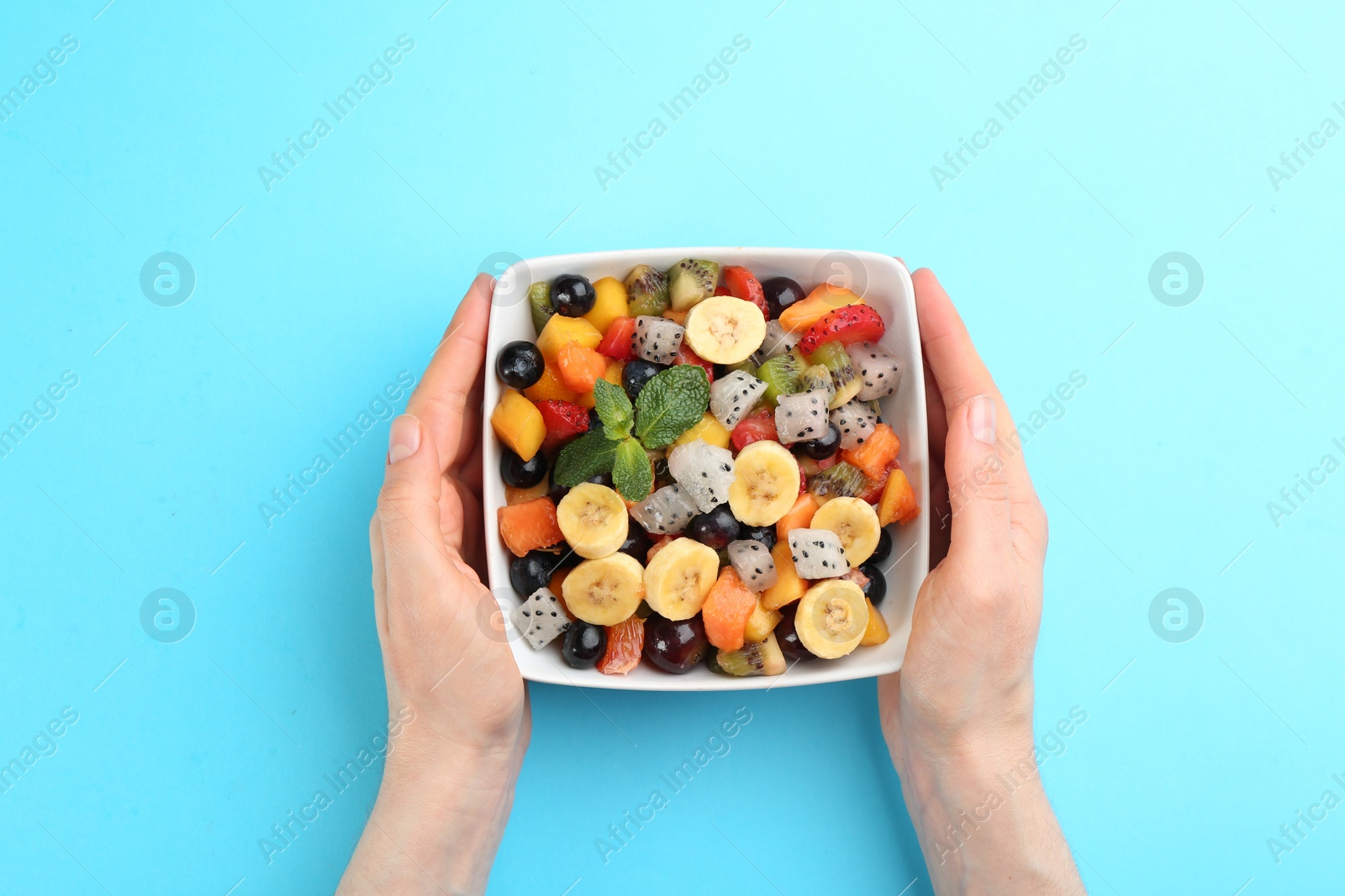 Photo of Woman with delicious exotic fruit salad on light blue background, top view