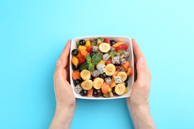 Woman with delicious exotic fruit salad on light blue background, top view