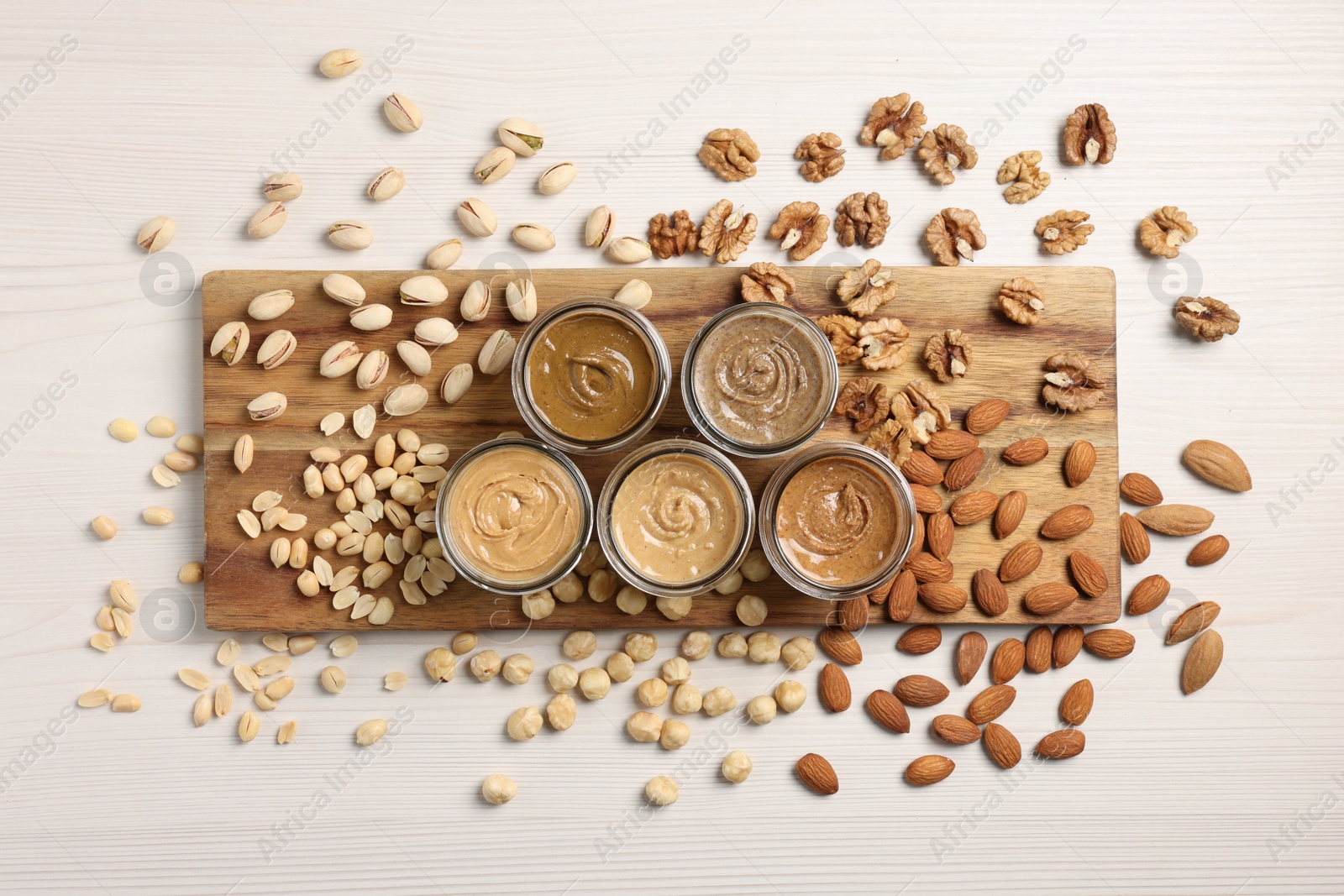 Photo of Many tasty nut butters in jars and nuts on white wooden table, flat lay