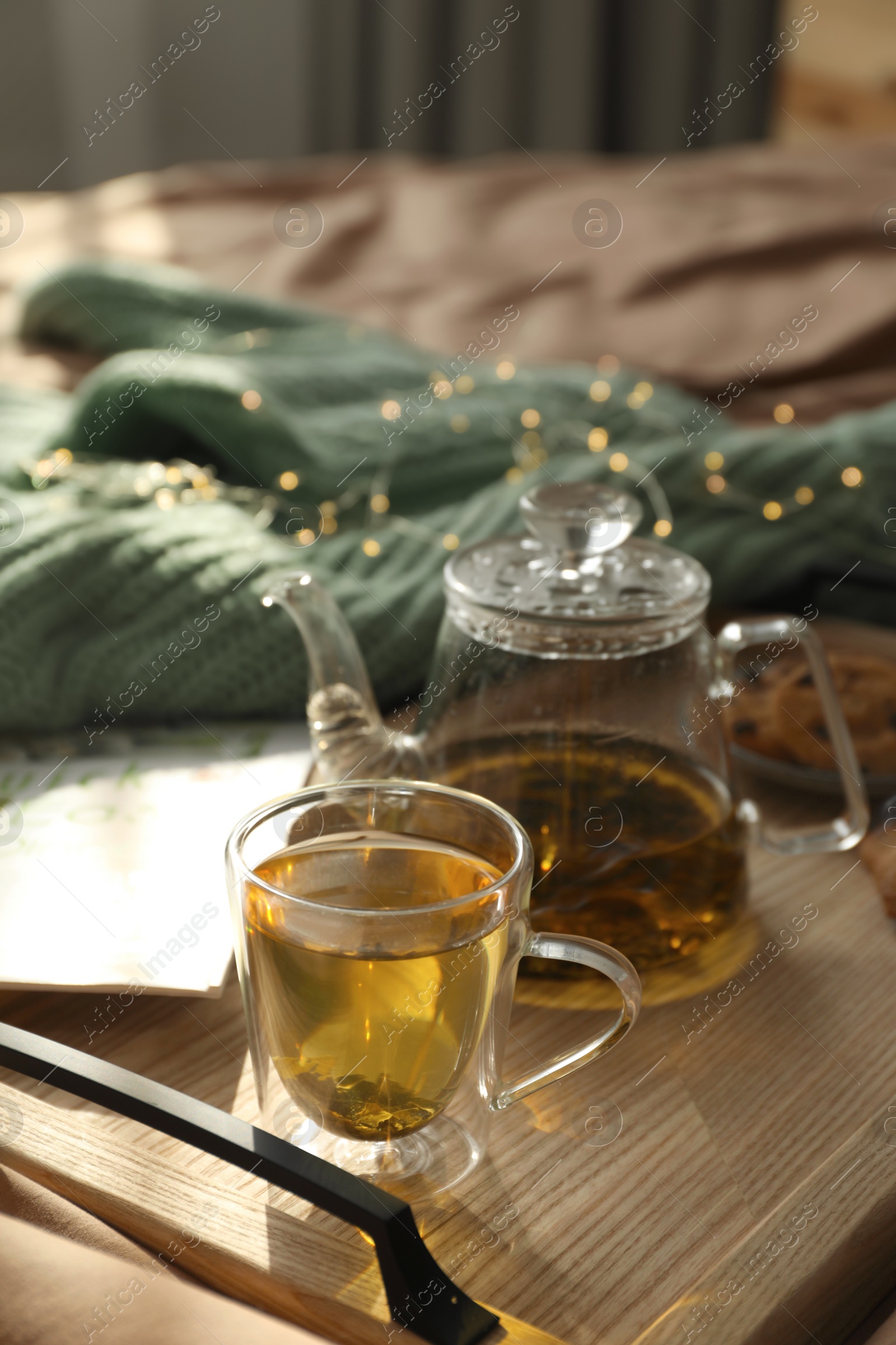 Photo of Wooden tray with freshly brewed tea on bed in room. Cozy home atmosphere