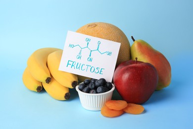 Photo of Card with word Fructose, delicious ripe fruits, blueberries and dried apricots on light blue background