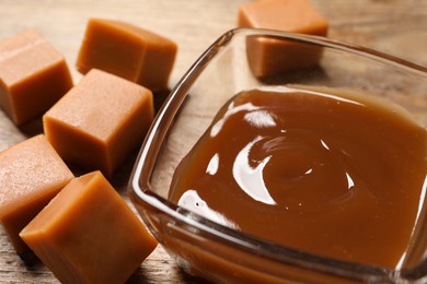 Photo of Tasty salted caramel in bowl and candies on wooden table, closeup