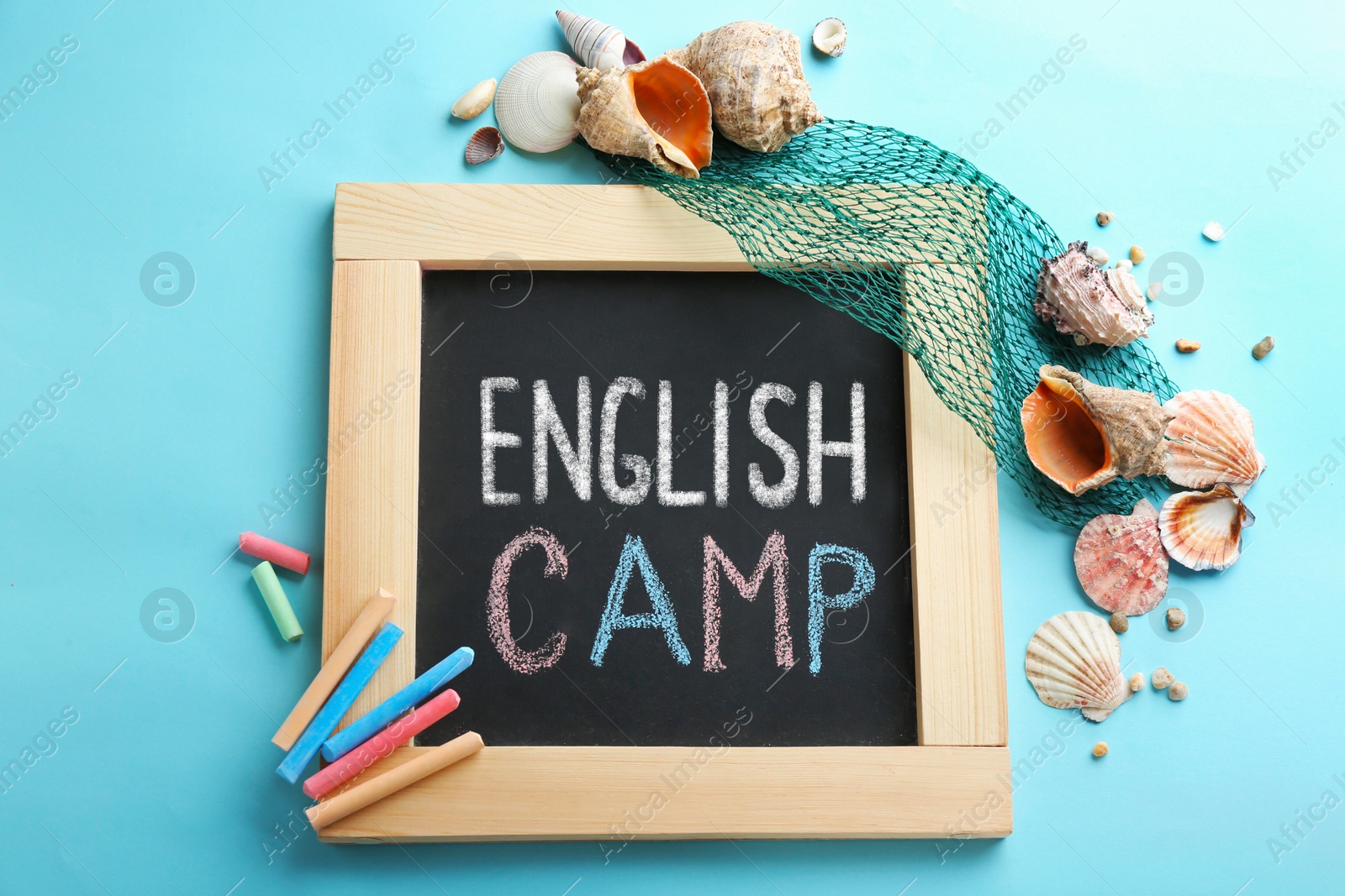 Image of Blackboard with words ENGLISH CAMP, colorful chalk and shells on blue background. Flat lay