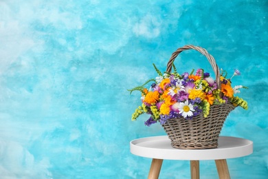 Photo of Wicker basket with beautiful wild flowers on table against color background