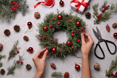 Florist making beautiful Christmas wreath at grey table, top view