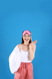 Young woman with pillow and sleep mask on blue background