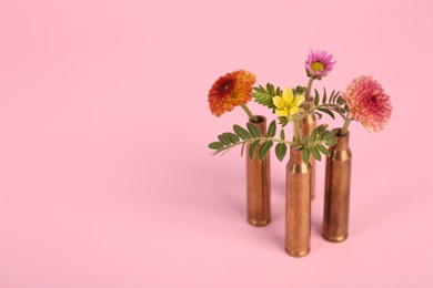 Photo of Bullet cartridge cases and beautiful flowers on pink background, space for text
