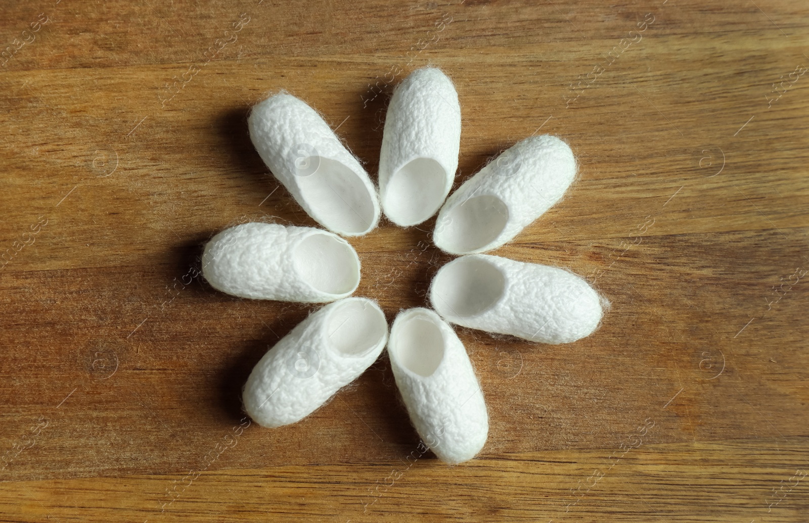 Photo of White silk cocoons on wooden table, flat lay