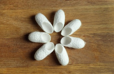 White silk cocoons on wooden table, flat lay