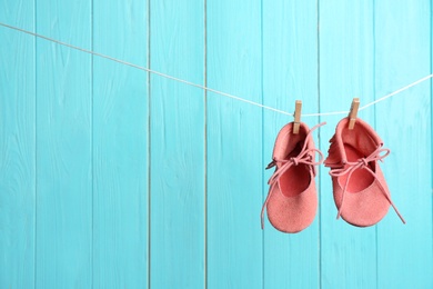 Photo of Baby shoes on laundry line against color wooden background, space for text. Child accessories