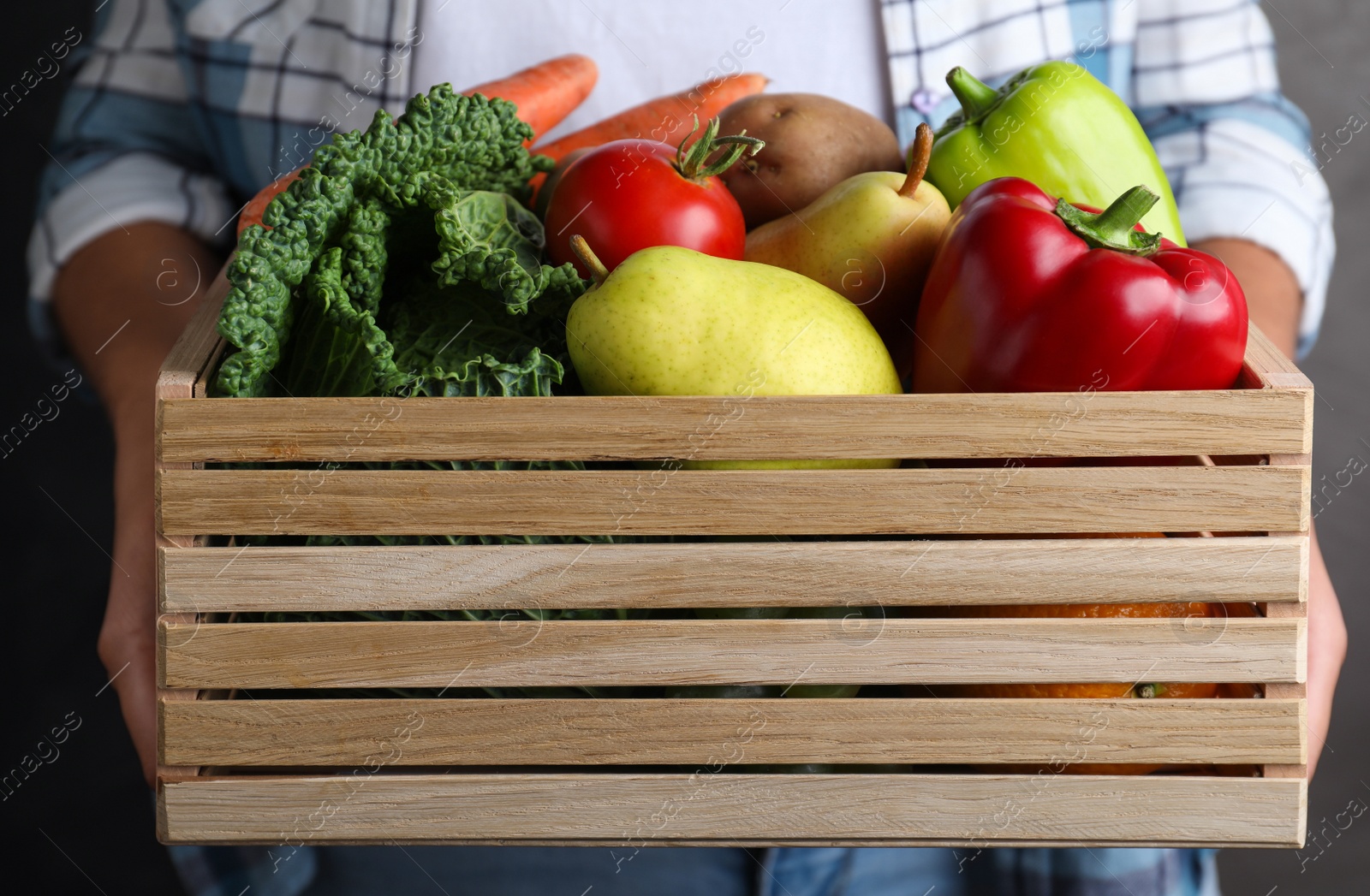 Photo of Farmer holding wooden crate filled with fresh vegetables and fruits on grey background, closeup