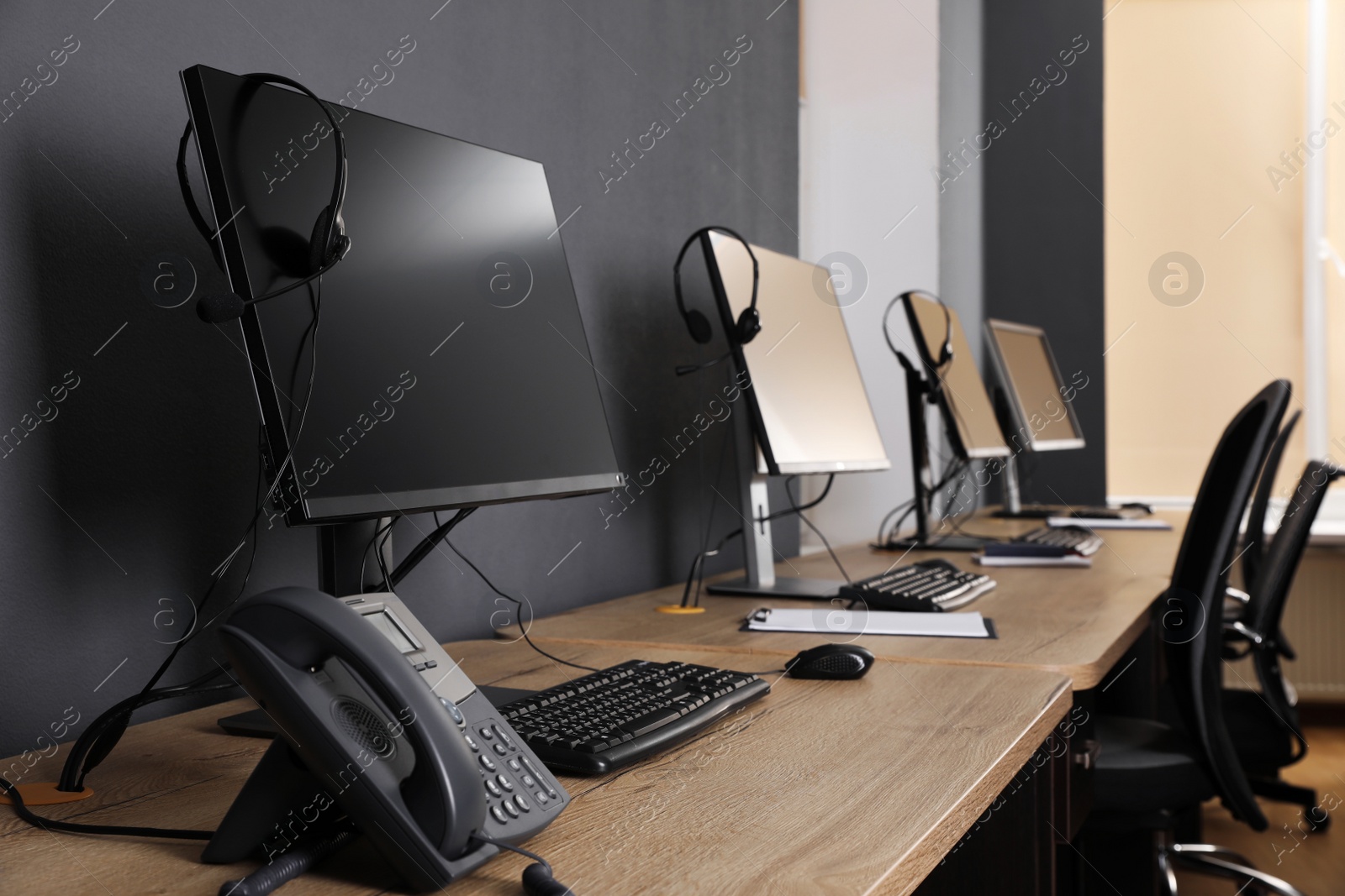 Photo of Stationary phone near modern computer with headset on wooden desk in office. Hotline service