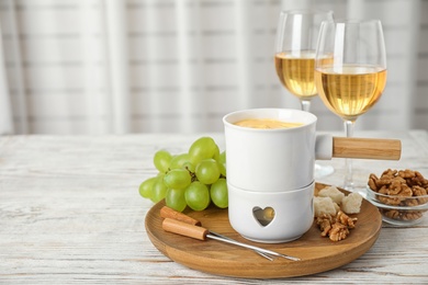 Pot of tasty cheese fondue served on white wooden table indoors, space for text