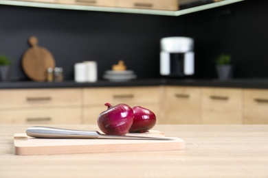 Board with fresh onion and knife on wooden table in kitchen. Space for text